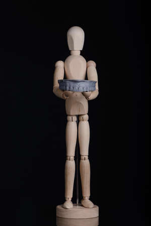 Human wooden figure holds in hands a dental upper jaw model printed on 3d printer on a black background.の写真素材
