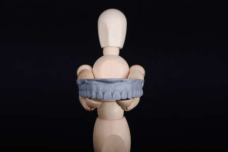 Human wooden figure holds in hands a dental upper jaw model printed on 3d printer on a black background.の写真素材