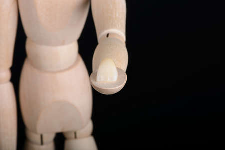 Human wooden figure holds in hands a zirconia bridge with glazour on a black background.の写真素材