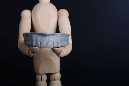 Human wooden figure holds in hands a dental upper jaw model printed on 3d printer on a black background.の写真素材