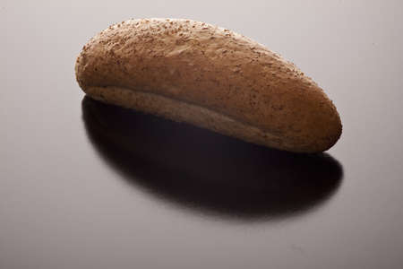 A single freshly baked wholewheat bread roll on a dark background with reflection and copyspace