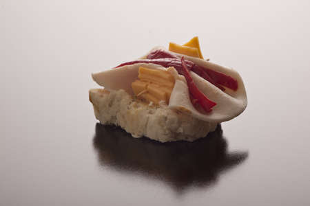 Tasty ham, pimento and cheese appetiser on sliced baguette against a dark reflective studio background with copyspaceの写真素材