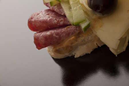 Closeup of thinly sliced rolled salami and cheese sandwich with cucumber on fresh white breadの写真素材