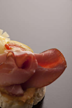 Thinly sliced smoked ham served on a slice of a baguette against a neutral studio background with...