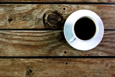 White cup with black coffee on brown wooden background. View from above.の写真素材