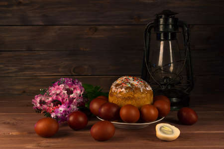 Easter cake, Easter eggs, lilac branches and a kerosene lamp on a wooden tableの写真素材