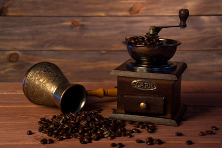 Vintage coffee grinder, turk copper coffee pot and coffee beans on brown wooden background