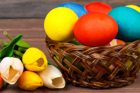 Easter eggs in wicker basket, red and yellow tulips on wooden boardsの写真素材