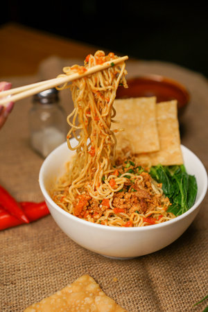 Chinese noodles with vegetables and meat in a bowl on a wooden tableの写真素材