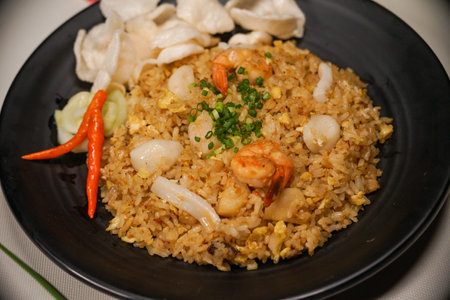 Fried rice with shrimp and vegetables in a black plate on the tableの写真素材