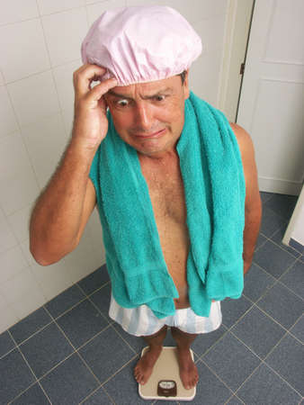 Man looking worried while standing on a weighing scaleの写真素材