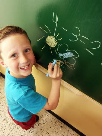 Happy school boy scribbling on blackboard in a classroomの写真素材