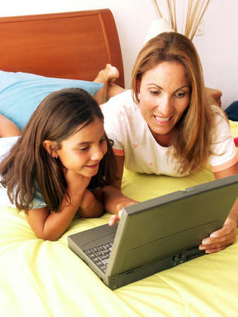 Hispanic mother and daughter looking at laptop while lying on bedの写真素材