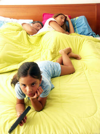 Hispanic girl watching tv while her parents are asleep on bedの写真素材