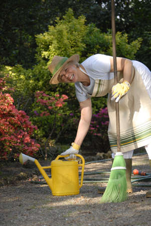 Elderly woman gardening while picking up a watering canの写真素材