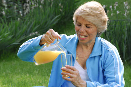 Elderly woman pouring a glass of orange juiceの写真素材