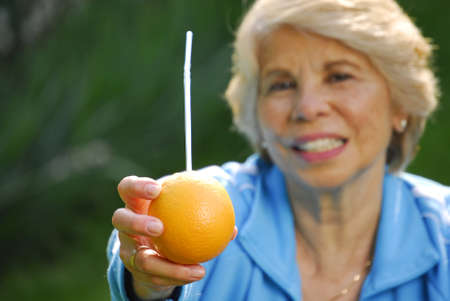 Elderly woman drinking orange juice from a fruitの写真素材