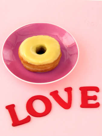 Doughnut with icing on a plate and the word love on backgroundの写真素材