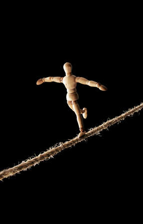 Wooden doll walking on a rope isolated on black backgroundの写真素材