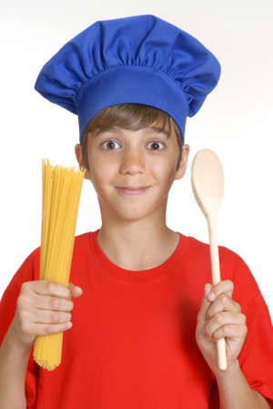 Young boy holding uncooked spaghetti and wooden spoonの写真素材