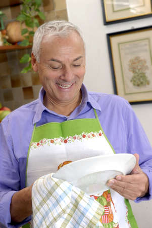 Senior man with apron wiping plateの写真素材