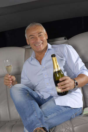 Senior man traveling in car with glass and a bottle of champagne
