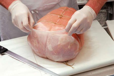 Butcher is removing the wrap on a prosciutto ham portionの写真素材