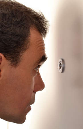 Surprised happy  young man looking out through the peephole of his front door.の写真素材