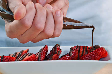 Adding dark chocolate cream on strawberries. Chocolate syrup on strawberries.の写真素材
