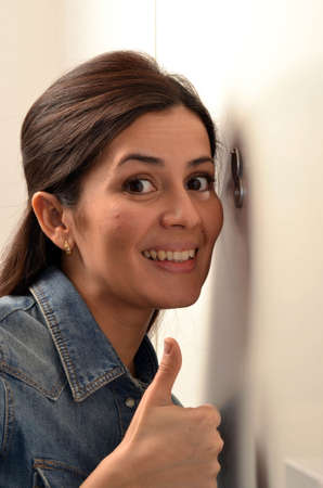 Surprised young woman looking out through the peephole of her front door.の写真素材