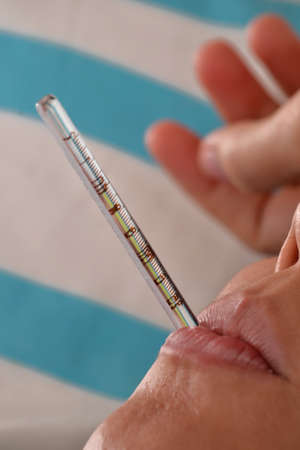Sick Young woman lying down on bed using a thermometer measuring fever.