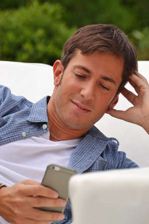 Young man chatting on smart phone lying down on outdoor sofa