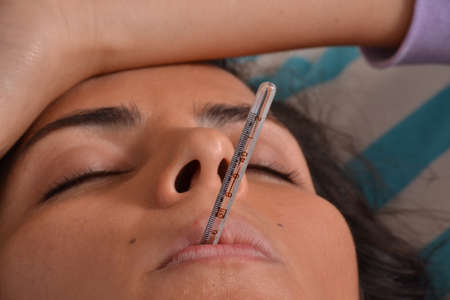 Sick Young woman lying down on bed using a thermometer measuring fever.の写真素材