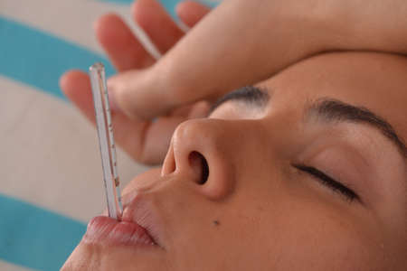 Sick Young woman lying down on bed using a thermometer measuring fever.の写真素材