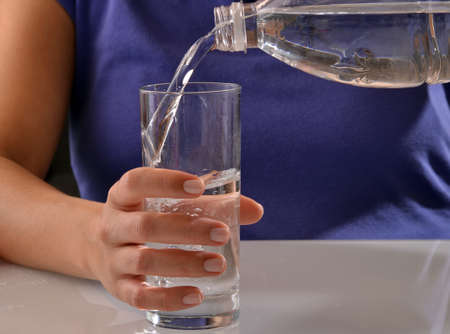 Young woman pouring potable water on a glass.