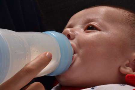 Mother feeding baby boy with a plastic baby bottle.