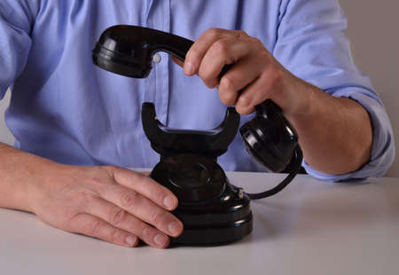 Man holding an old black telephone receiving a call, lift telephone handset.の写真素材