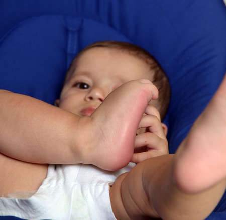 Baby boy portrait holding his feet.