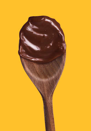 Melted dark chocolate wood spoon isolated on yellow background.の写真素材