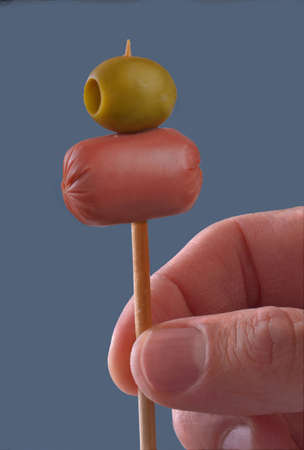 Hand holding sausage and olive on wooden stick for snack party.の写真素材
