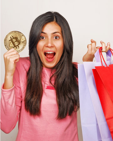 Happy young woman holding shopping bags and bitcoin cryptocurrency token.の写真素材