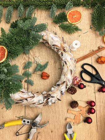 Christmas wreath on wooden table top view. Top down view of florist's worktable. Making of Christmas wreath. Getting ready for Christmas. Christmas tree decoration toys, gift box and scissors over rustic wood table background, top viewの写真素材