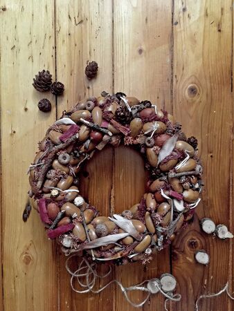 Rustic wreath with dry acorns, cones on a dark brown wooden background, sunny autumn day. House decoration.の写真素材