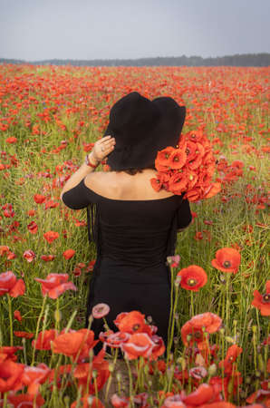 Girl with black hat in a poppy field. A womanstands in a flower garden. A girl walks in a meadow with beautiful red flowers.の写真素材