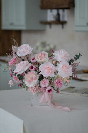 Beautiful bouquet of peonies and pink roses on the table. In the background is the interior of a modern white kitchen. Concept of home comfort.の写真素材