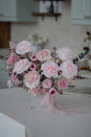 Beautiful bouquet of peonies and pink roses on the table. In the background is the interior of a modern white kitchen. Concept of home comfort.の写真素材