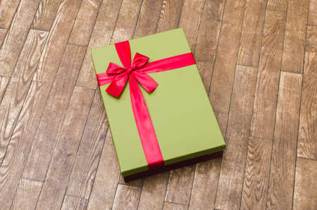 green gift box with red ribbon on wooden background