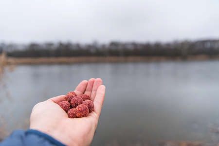 Man holds fish lure in nature near pond. He prepares to fishの写真素材