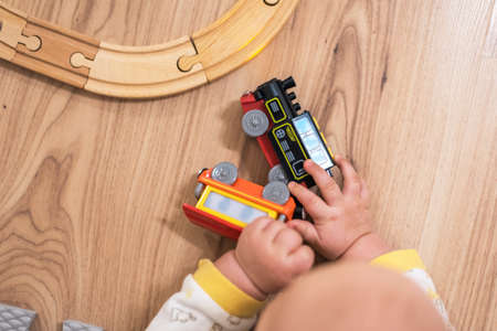 Baby is playing with small wooden train on the floorの写真素材