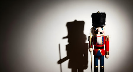 A traditional wooden nutcracker toy soldier in a red uniform stands in a spotlight, creating a large, imposing shadow on the background wall. A classic Christmas decoration.の素材